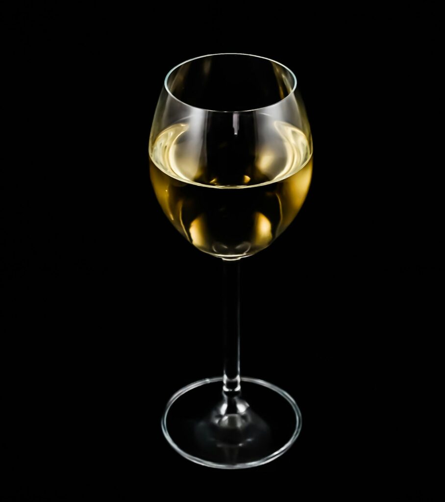 A single glass of white wine elegantly displayed against a black background.